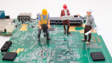Miniature construction figures are posed working on a motherboard of a computer to show the idea of engineers building technology. 