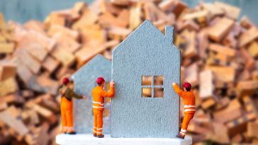 A photo of miniature figures building a small cut out of a house to show the idea of real estate tech developer teams working together. 
