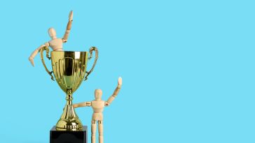 Wooden figures pose next to a gold trophy to show the idea of employee recognition.