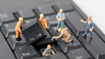 A photo of mini figures repairing a computer keyboard to show the idea of engineers working on technology. 