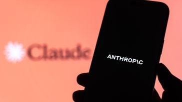 A hand holds a smartphone reading "Anthropic" in front of the Claude logo.