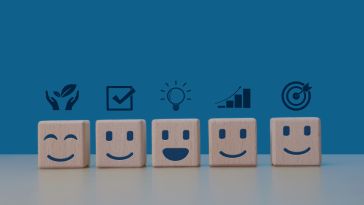 An image of wooden blocks with smiling faces and icons to show the idea of employee wellbeing. 