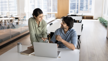 Two engineers discuss a project together while working in an office.