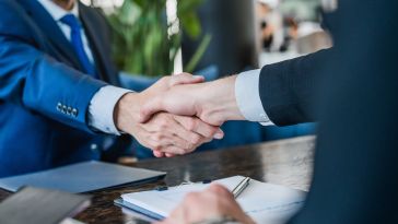 A close up of a handshake between two people wearing business suits.