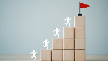 An image of blocks in a pyramid with people icons running up them to a red flag to show the idea of career growth. 