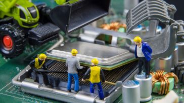 A photo of miniature construction figures working on a motherboard to show the idea of an engineering team building software. 