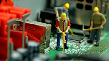 A photo of miniature construction figures working on a motherboard to show the idea of an engineering team working together to build software. 
