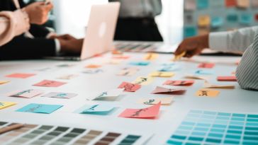 Several colleagues place sticky notes on a table while brainstorming ideas in an office.