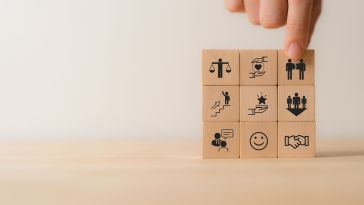 A photo of stacked blocks with icons like a smiley face, handshake, and a person ascending stairs to show the idea of inclusive hiring and onboarding at a workplace. 