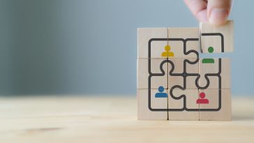 A photo of wooden blocks with images of puzzle pieces and people icons to show the idea of building a company culture that fits with employee satisfaction.