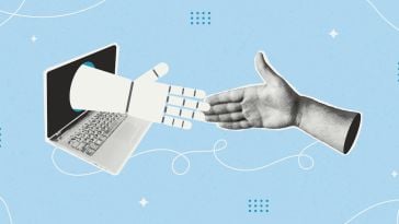 A human hand reaches out to a robotic hand coming out of a laptop screen.