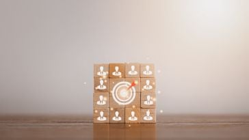 Wooden blocks stacked in a photo with images of people and a target with a bullseye in the middle to show the idea of leaders keeping a team on target. 