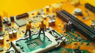 A photo of miniature figures working on an open computer hard drive to show the idea of tech professionals using AI to improve their work flows. 