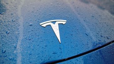 A Tesla logo in the front hood of a Tesla vehicle soaked in rain.