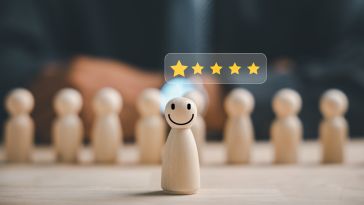 A photo of wooden figures with one in the foreground with a smile and five stars above its head to show the idea of a happy employee. 