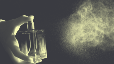 A hand sprays a bottle of perfume