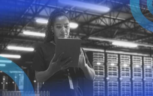 A woman looks at a tablet in front of a row of servers