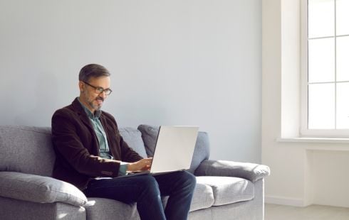 A man is on a couch doing work on a laptop.