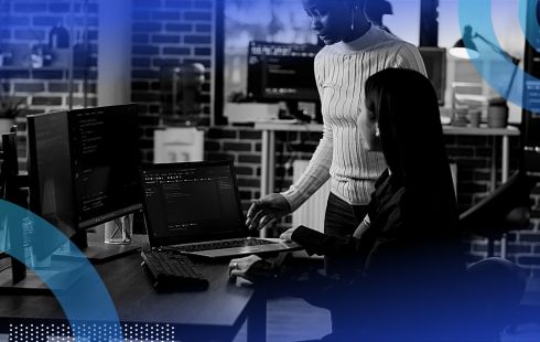 Two women work on code on a multiple monitor setup