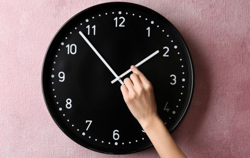 A hand sets the hour hand on a black wall clock.