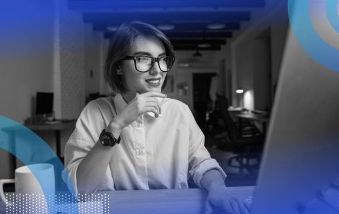 A woman in tech looking happy and sitting at a desk in front of a computer screen.