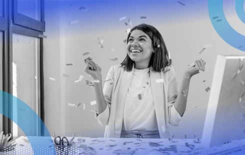 A business woman sitting at a computer desk, smiling with confetti raining down on her.