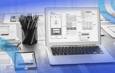 A laptop computer displays a UX design display with a cup of pencils and a smartphone alongside