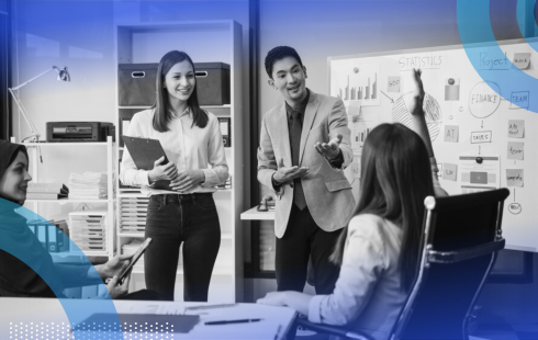 A young woman raising her hand in a meeting while team members smile at her and the leader calls on her.