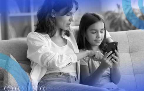 A mother and child sitting on a couch interacting with a smartphone together.