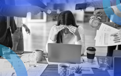 A woman hunched over her laptop shielding her face from several colleagues shoving clocks and papers at her.