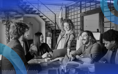 A group of young professionals laughing and exchanging ideas, with the woman in the middle of the group raising her arm triumphantly in the air.