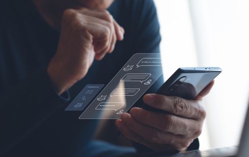 A man uses a smartphone and a rendering of a conversation with a chatbot hovers above the screen.