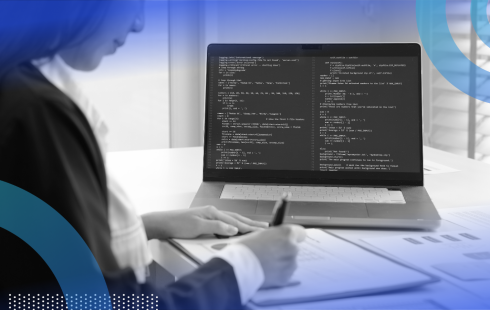 A developer works on a laptop full of code and writes in a notebook