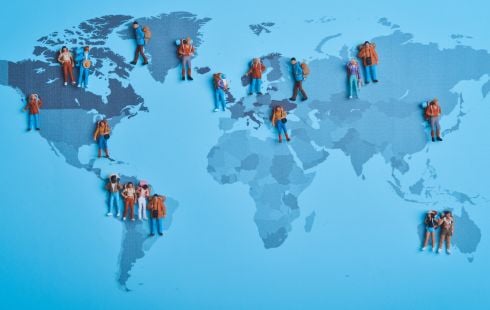 A photo of a flat top view of miniature travellers spread around on a world map to show the idea of remote work. 