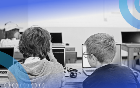 Two kids work on laptops in a classroom
