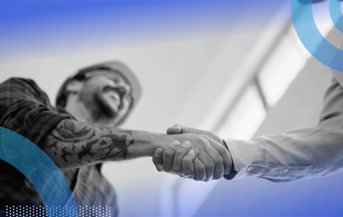 A man in a hardhat and flannel shirt shakes hands with a man in a dress shirt