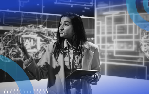 A woman presenting on a stage with a futuristic, high-tech digital background.
