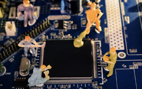 A photo of miniature figures working on a computer motherboard to show the idea of engineers working on AI.
