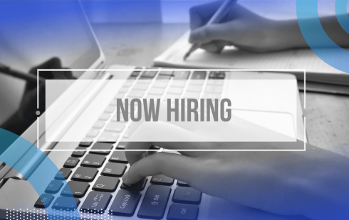 A closeup on hands typing on a laptop keyboard with a Now Hiring sign atop