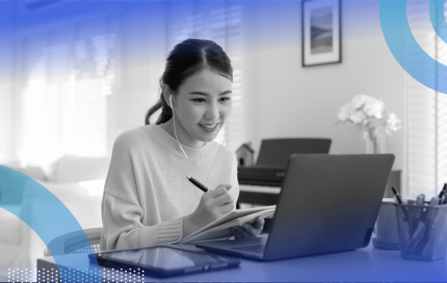 A young woman works on a laptop and writes in a notepad