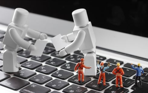A photo of toy workers and two larger toy robots on a keyboard to show the idea of engineers building AI.