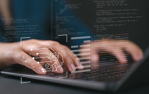 A close up of hands typing on a laptop with holographic images of code and AI icons floating in the foreground.