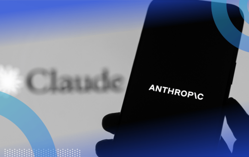 A hand holds a smartphone with the Anthropic logo in front of a screen advertising the company's Claude tool.