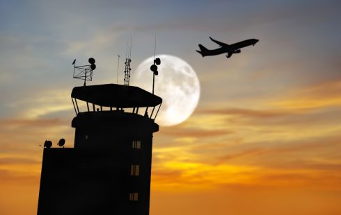 An airpline flies over a Terminal Radar Approach Control (TRACON) tower.