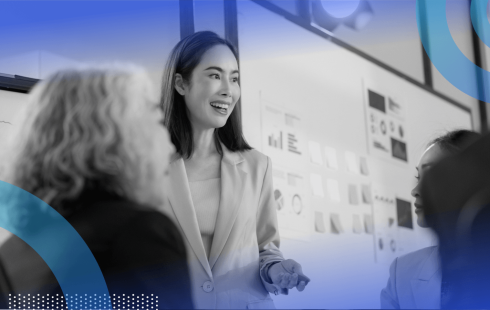 A woman in a business suit stands in front of a kanban board and makes a presentation
