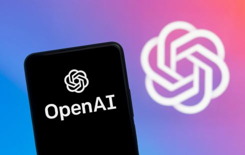 A smartphone with the OpenAI logo is pictured in front of a larger image with the OpenAI logo.