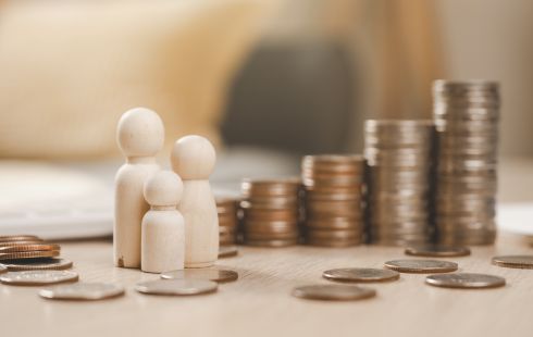 Three wooden figures next to piles of coins to show the idea of competitive compensation and holistic perks that support work-life balance for Academia.edu employees. 