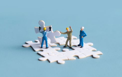 A photo of miniatures placing a puzzle piece into place to show the idea of team culture 