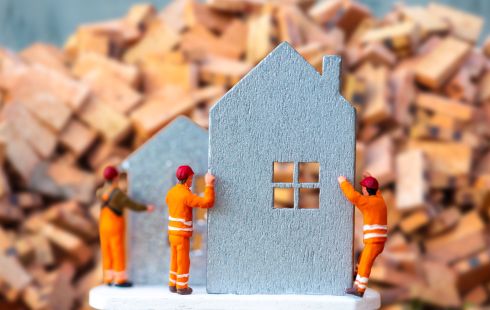 A photo of miniature figures building a small cut out of a house to show the idea of real estate tech developer teams working together. 