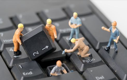 A photo of mini figures repairing a computer keyboard to show the idea of engineers working on technology.